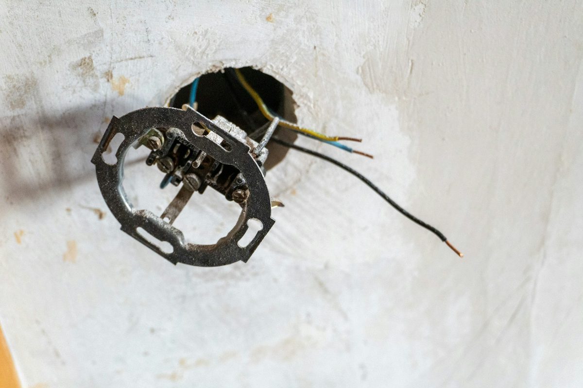 Een oud inbouwstopcontact hangt los uit de muur, met de draden nog aangesloten